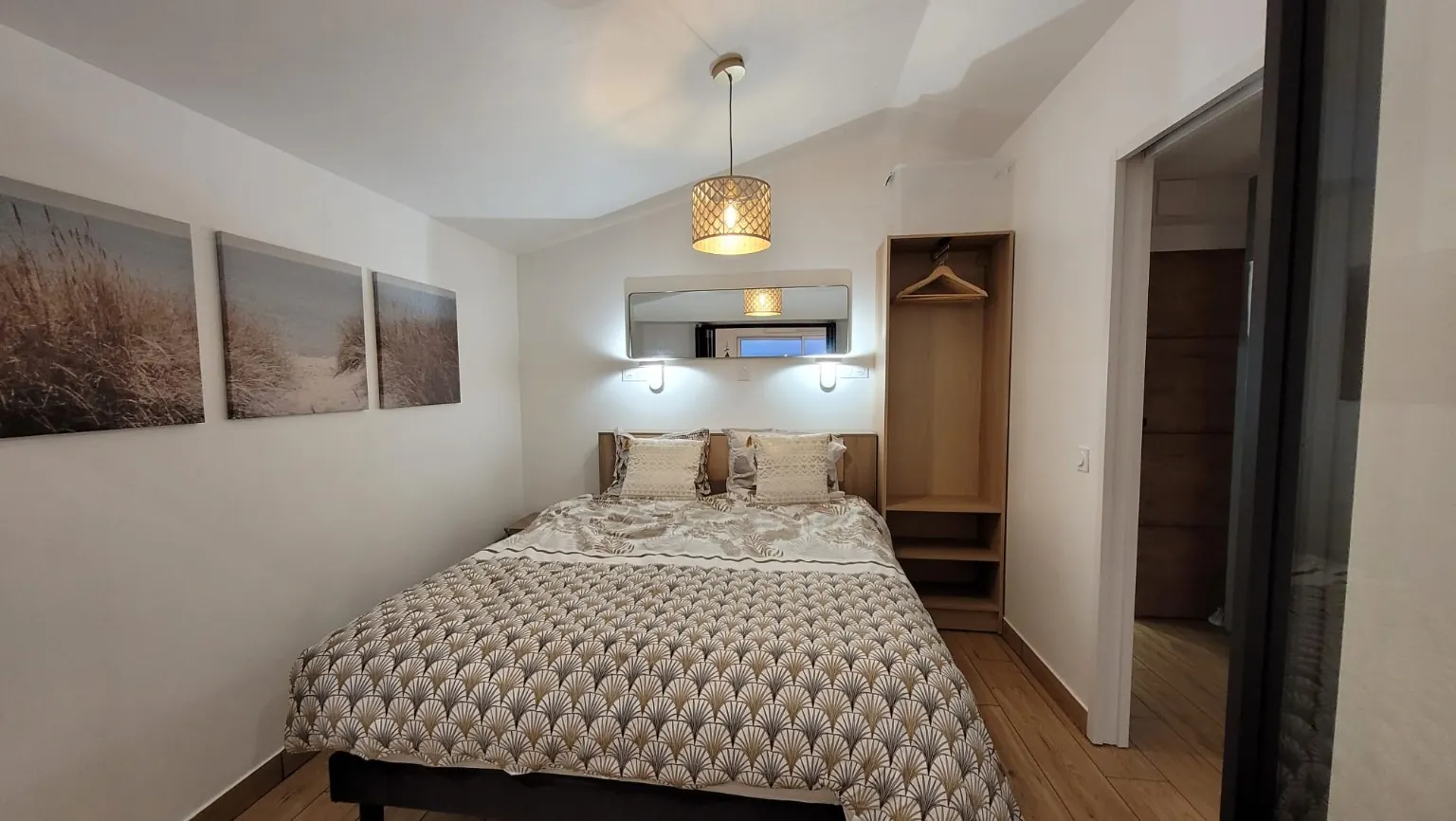 Chambre avec lit double, tête de lit en bois, penderie et décoration inspirée des dunes.