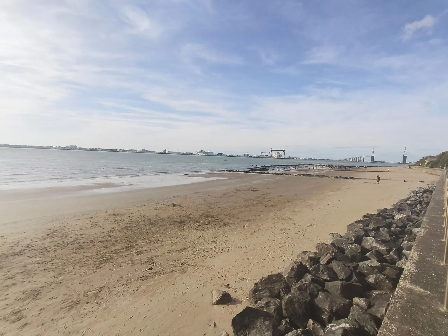 Vue des environs : plage de sable, estuaire et pont au loin, photographiés depuis le bord de mer.