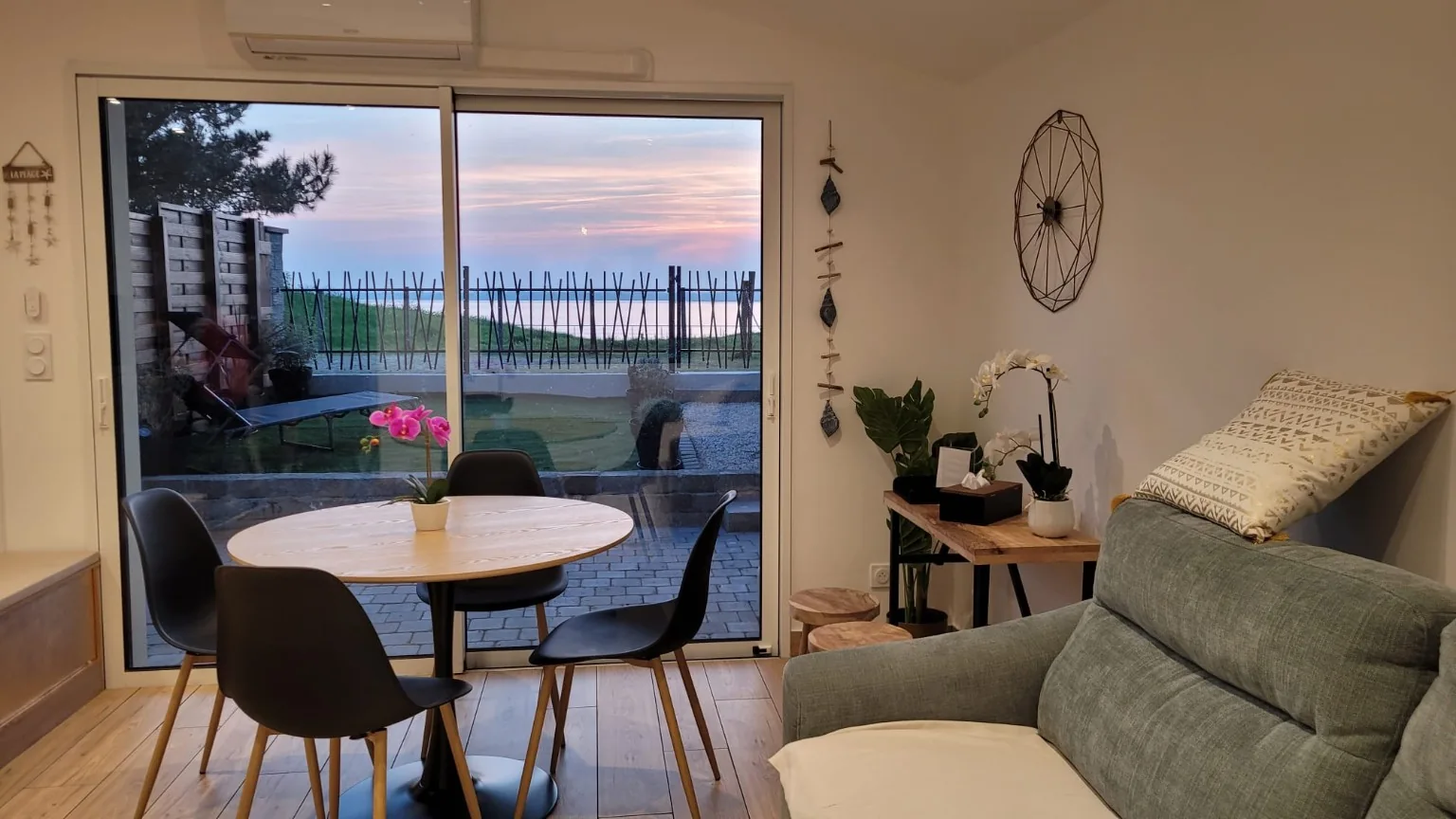 Vue depuis le séjour : table ronde, canapé et baie vitrée donnant sur le jardin et l’estuaire.