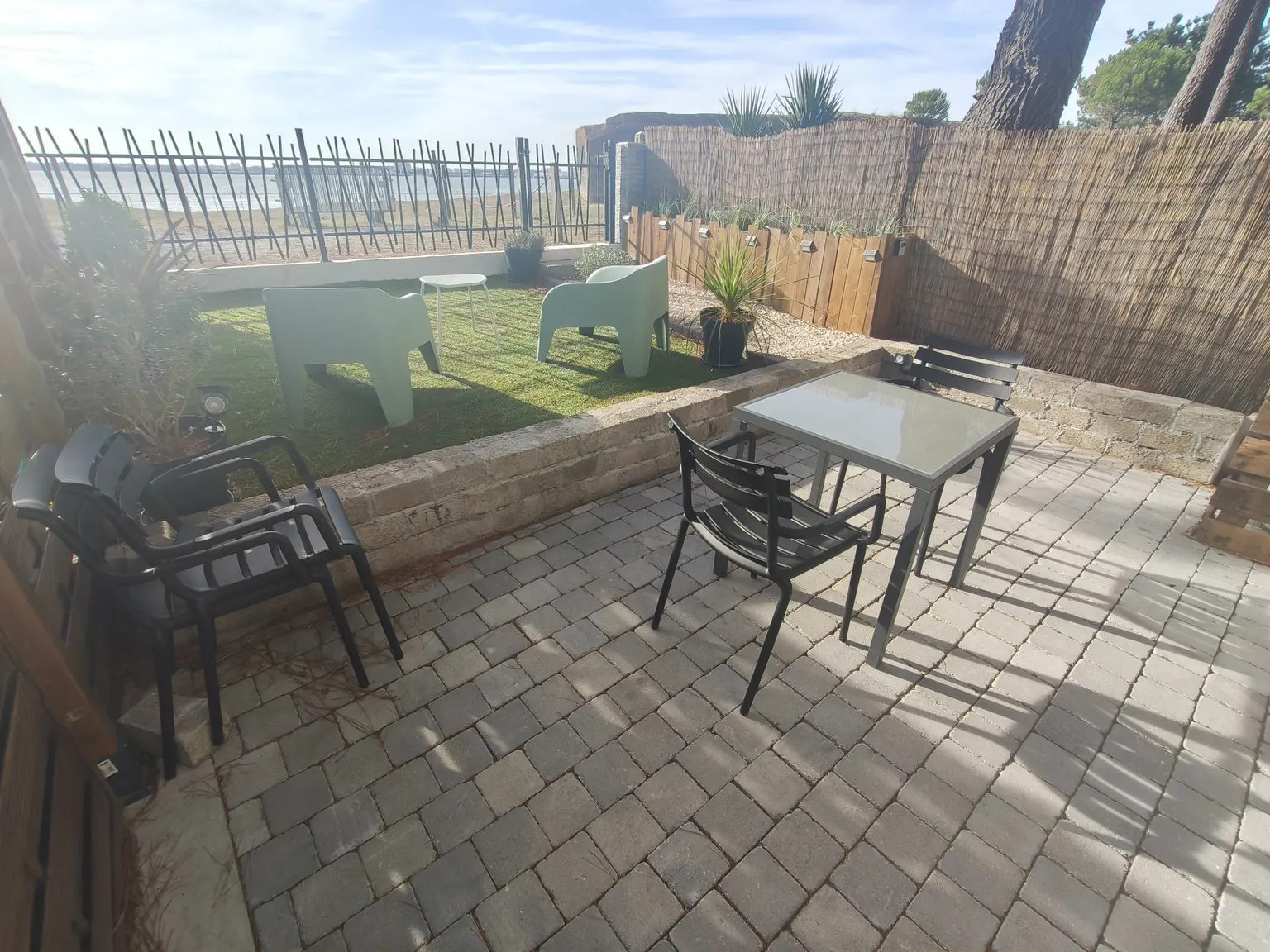 Terrasse pavée avec table et chaises, fauteuils dans le jardin et vue sur l’estuaire.